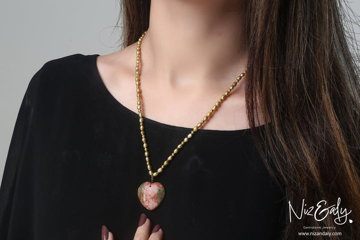 Niz & Aly unakite heart pendant on a golden rice pearl strand worn by a woman in a black top.