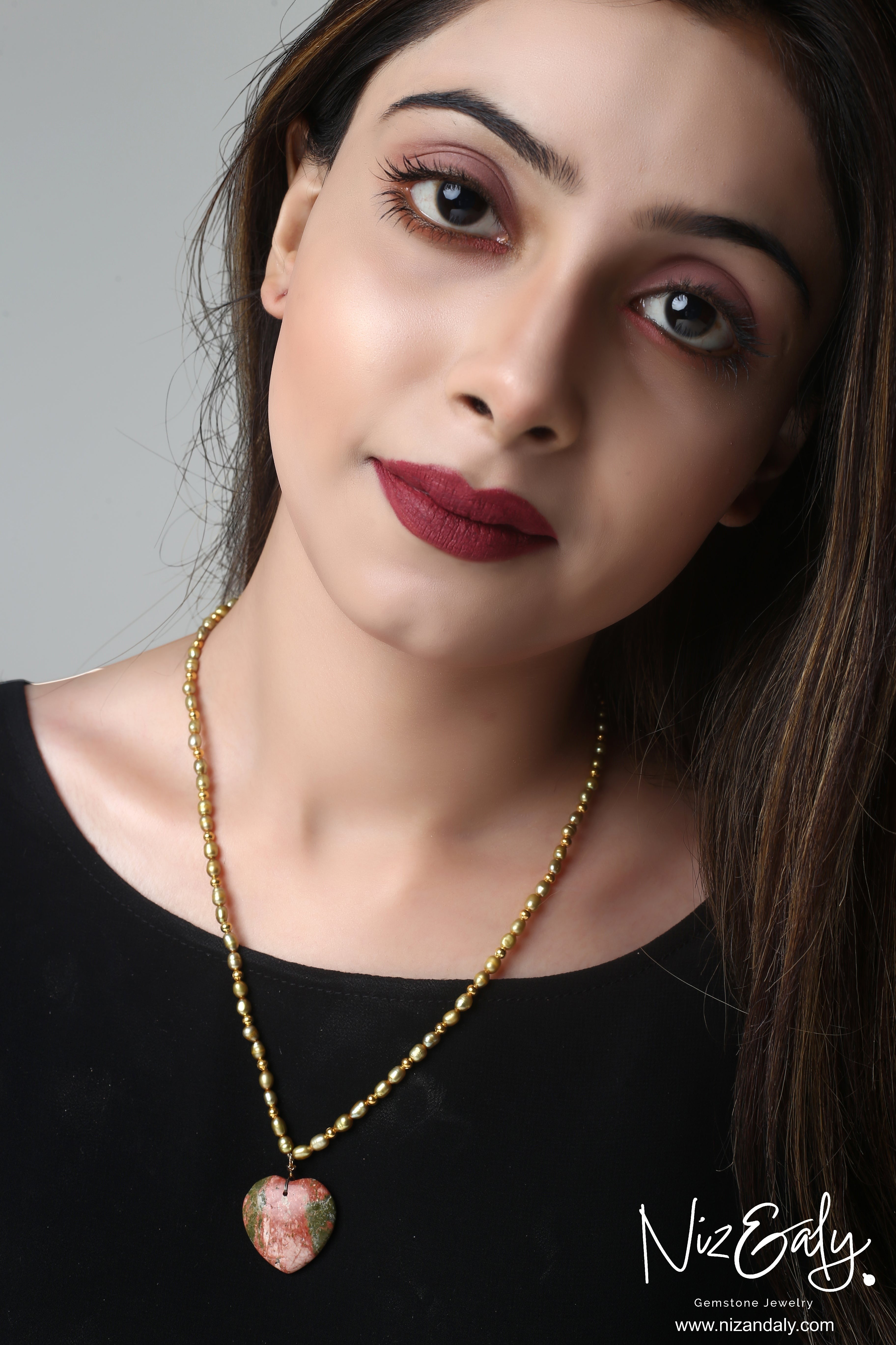 Niz & Aly unakite heart pendant on a golden rice pearl necklace worn by a woman.