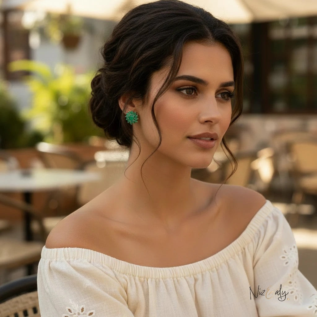 Niz & Aly vintage-inspired round green emerald stud earrings worn by a woman with an elegant updo in an outdoor cafe.