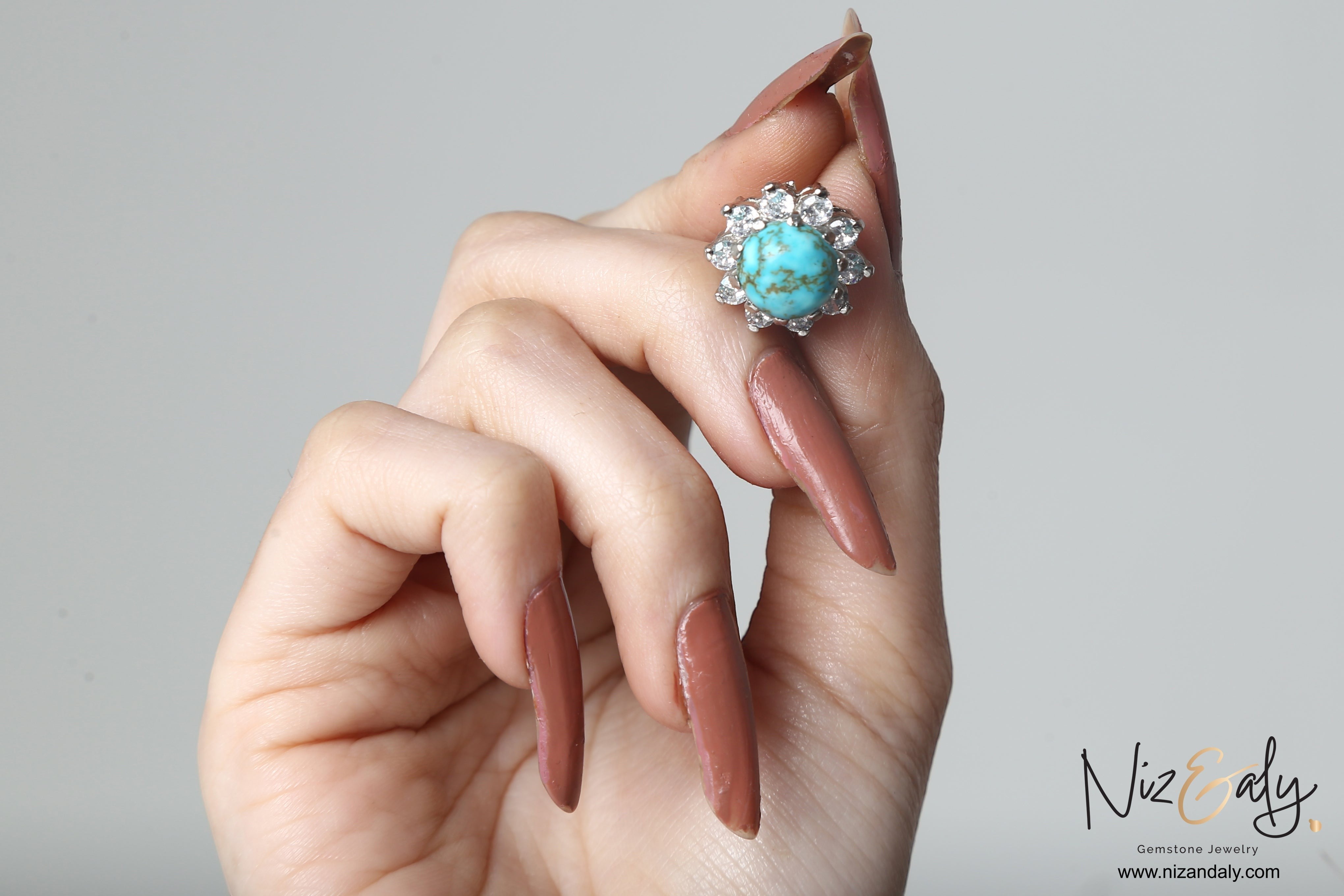 Niz & Aly round vintage blue Kingman turquoise ear stud with a halo of sparkling stones held in a hand