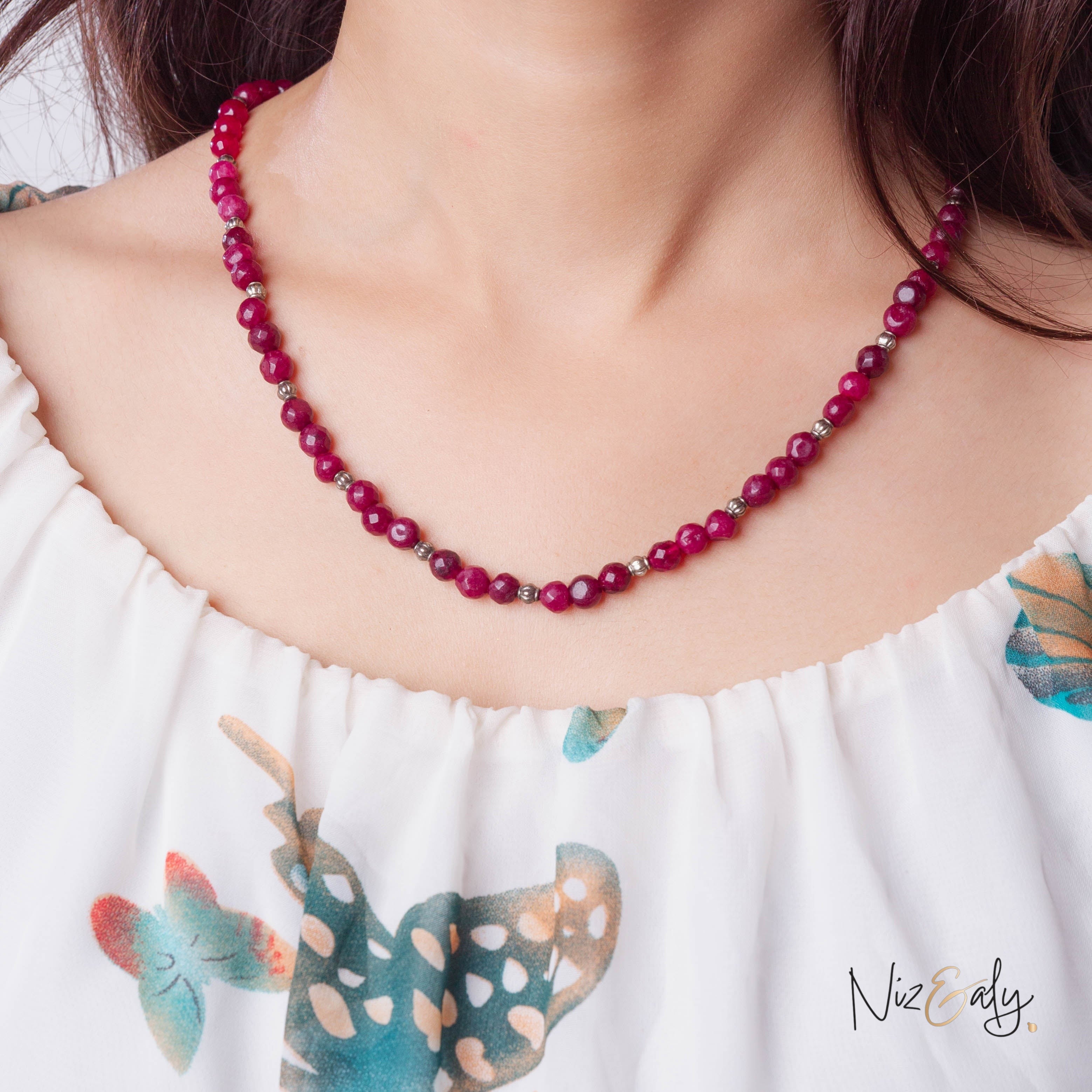 Niz & Aly faceted almandine garnet bead necklace worn on a woman in a white floral top
