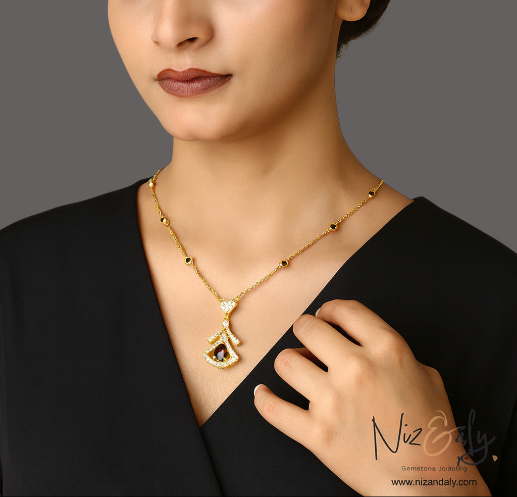 Niz & Aly Midnight Grace gold fan-shaped pendant necklace with a deep red garnet and shimmering clear stone accents.